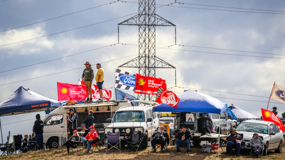 5 cars set up on a hill with people sitting around them in chairs and standing on top with holden flags flying.