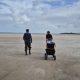 Two researchers walk a cart of sampling gear across wide sand flats beside the shallow water of the Coorong.