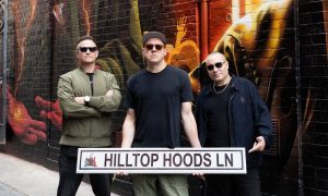 The three members of Hilltop Hoods holding a Hilltop Hoods Ln street sign in the painted laneway