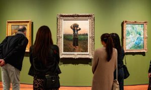 Gallery visitors standing in front of three framed paintings hung on a green wall