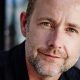 Actor Billy Boyd in a dark shirt, smiling beside a sunlit window